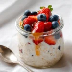 Fresh overnight oats with fruit and yogurt topped with berries and honey in a glass jar